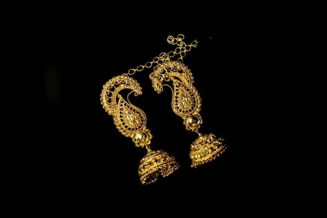 Pair of paisley gold jhumka earrings on black cloth
