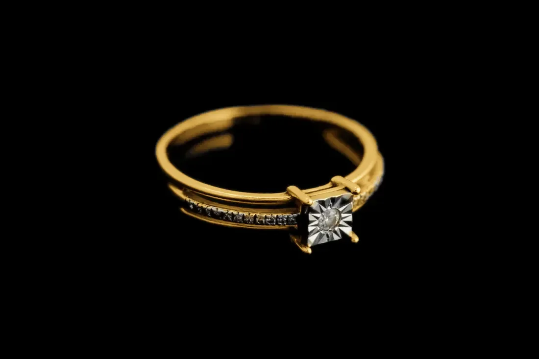 Gold solitaire ring with a diamond on a dark surface