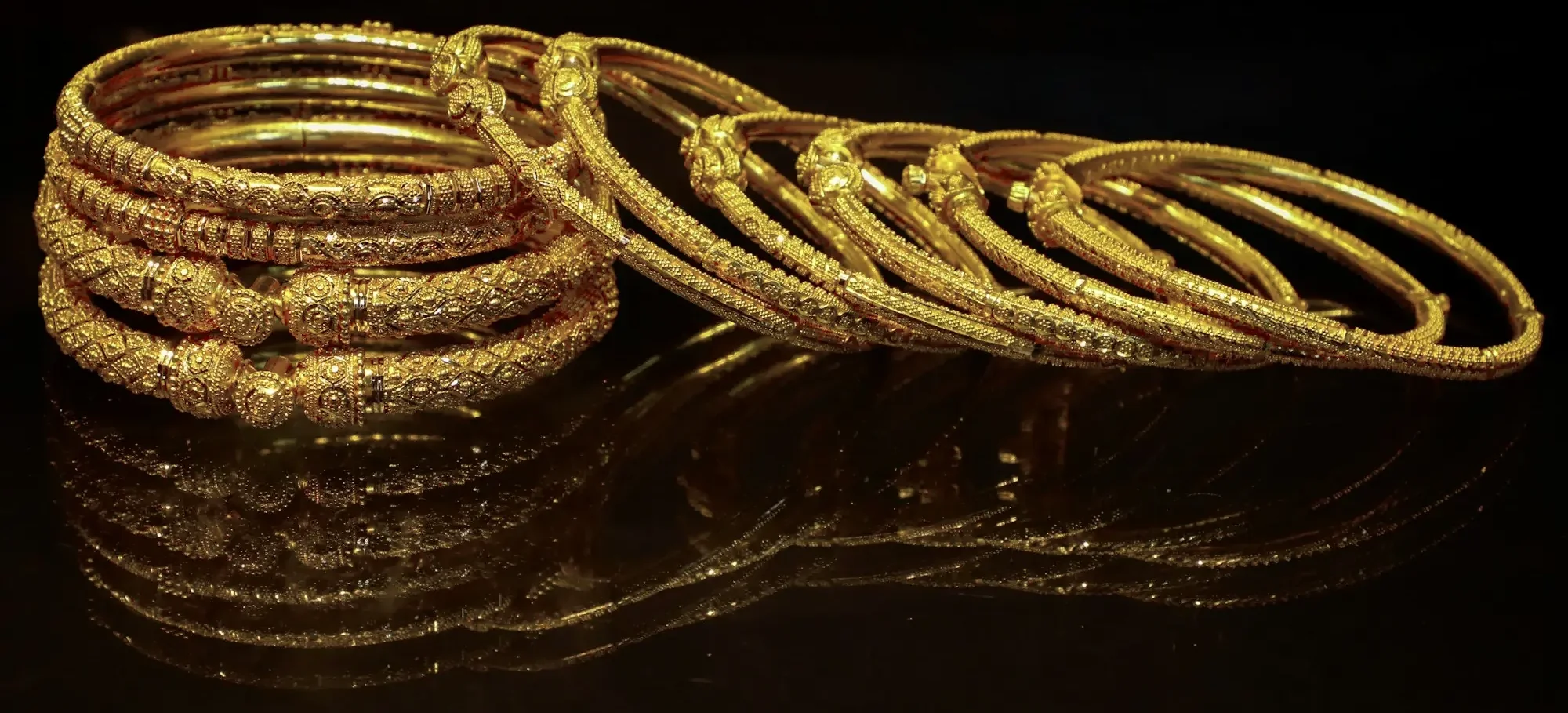 Stacks of gold bangles on a black surface